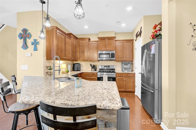 kitchen with stainless steel appliances, a peninsula, a sink, light wood finished floors, and brown cabinetry