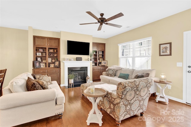 living area with ceiling fan, baseboards, wood finished floors, and a glass covered fireplace