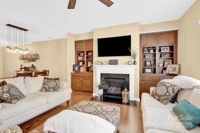 living area featuring light wood-style floors, ceiling fan, and a fireplace with flush hearth