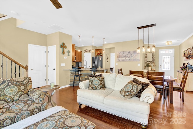 living room featuring crown molding, stairs, baseboards, and wood finished floors