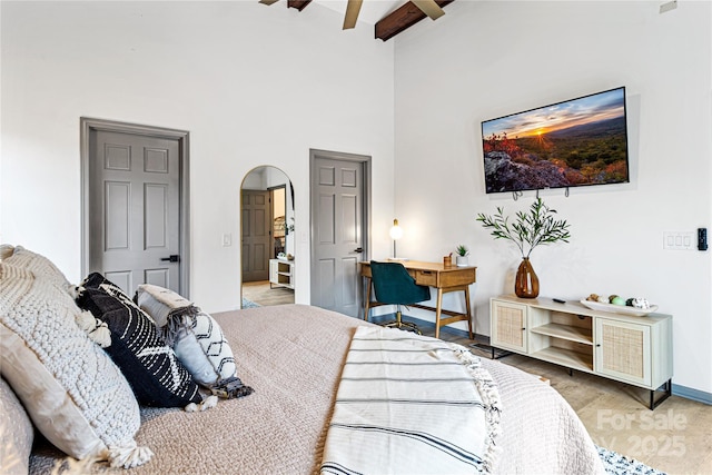 bedroom with arched walkways, beam ceiling, a towering ceiling, a ceiling fan, and baseboards