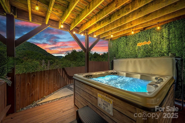 deck at dusk featuring fence and a hot tub