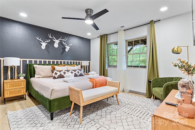 bedroom with an accent wall, visible vents, wood finished floors, and recessed lighting