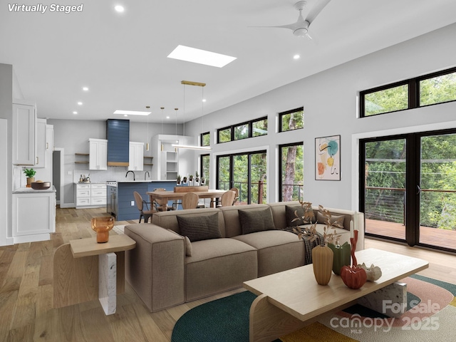 living room with a skylight, a ceiling fan, light wood-style flooring, a high ceiling, and recessed lighting