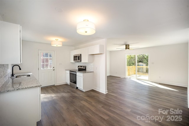 kitchen with light stone counters, stainless steel appliances, a sink, white cabinetry, and open floor plan