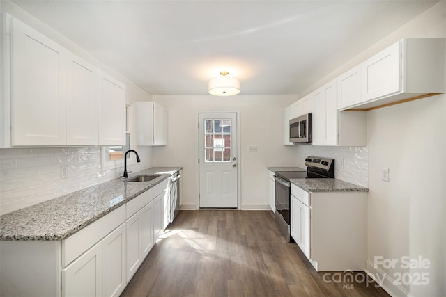 kitchen with a sink, baseboards, white cabinets, appliances with stainless steel finishes, and light stone countertops