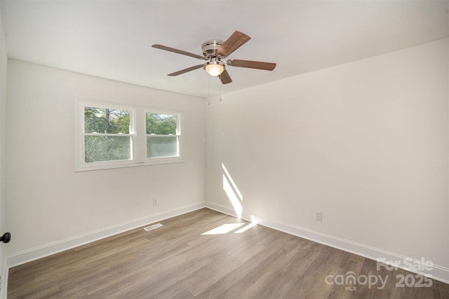 spare room featuring a ceiling fan, visible vents, baseboards, and wood finished floors