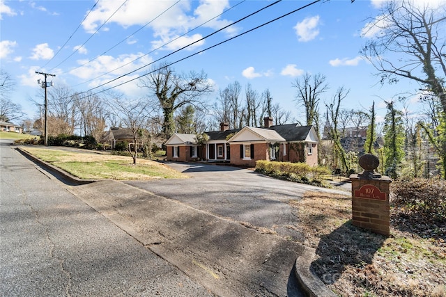 view of front of home featuring a chimney, aphalt driveway, and brick siding