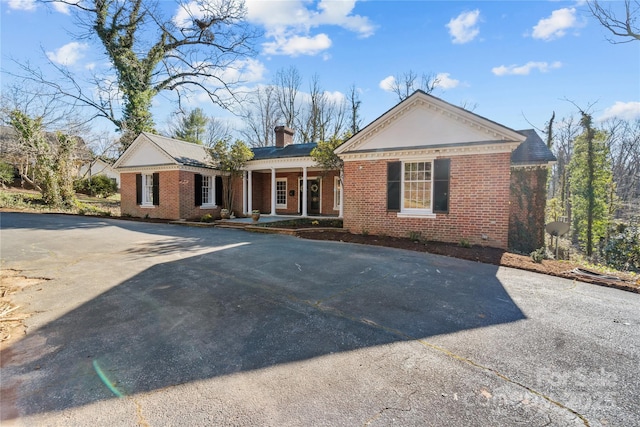 view of front facade with driveway, covered porch, a chimney, and brick siding