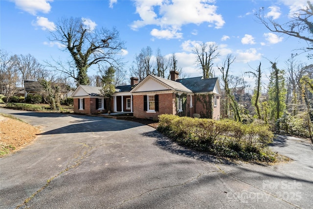 view of front of house featuring aphalt driveway, a chimney, and brick siding