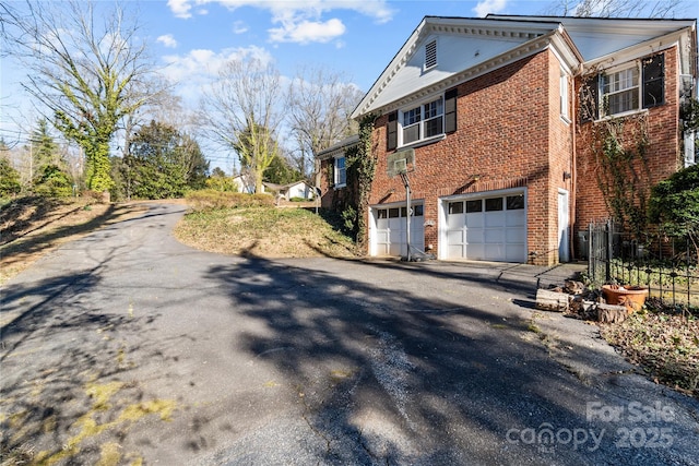 view of side of property featuring driveway, brick siding, an attached garage, and fence