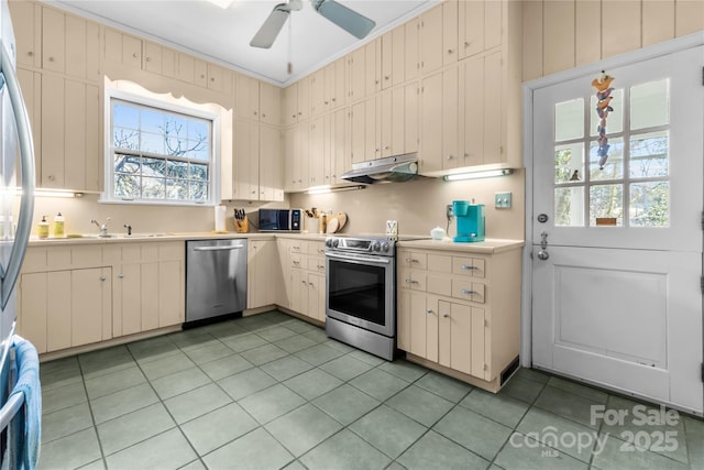 kitchen featuring crown molding, stainless steel appliances, light countertops, a sink, and under cabinet range hood