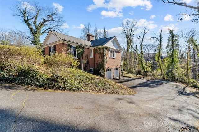 view of side of property with aphalt driveway, brick siding, a chimney, and an attached garage