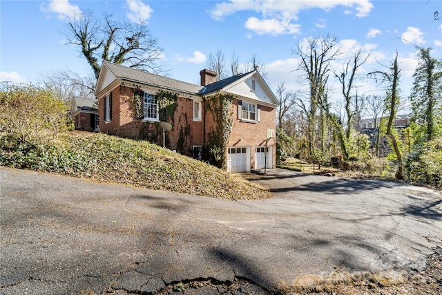 view of home's exterior with aphalt driveway, brick siding, a chimney, and a garage