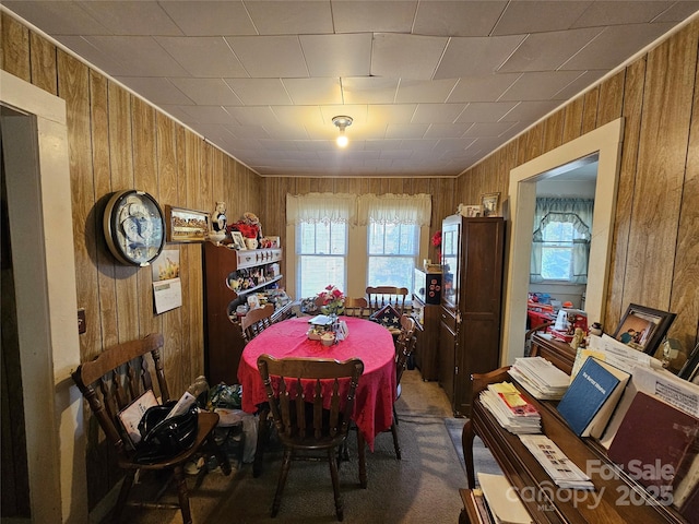 carpeted dining area featuring wood walls