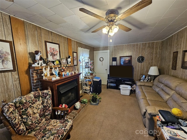 living room with a ceiling fan, a fireplace with raised hearth, wooden walls, and carpet flooring