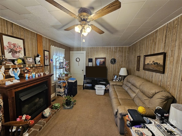 living room featuring carpet flooring, a fireplace with raised hearth, wood walls, and ceiling fan