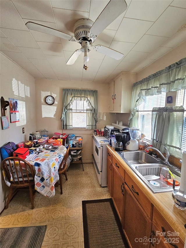 kitchen with electric stove, a ceiling fan, brown cabinets, light countertops, and a sink