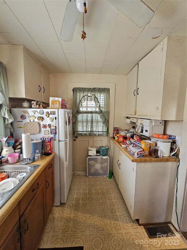 kitchen with white cabinets, light countertops, freestanding refrigerator, and brown cabinets