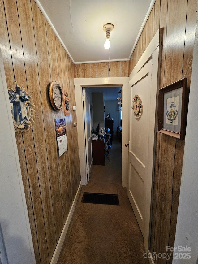 hall with crown molding, dark carpet, and wooden walls