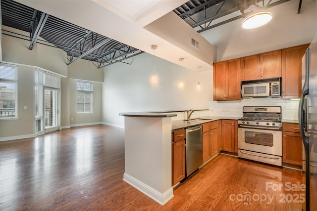 kitchen featuring a peninsula, a sink, open floor plan, appliances with stainless steel finishes, and brown cabinets