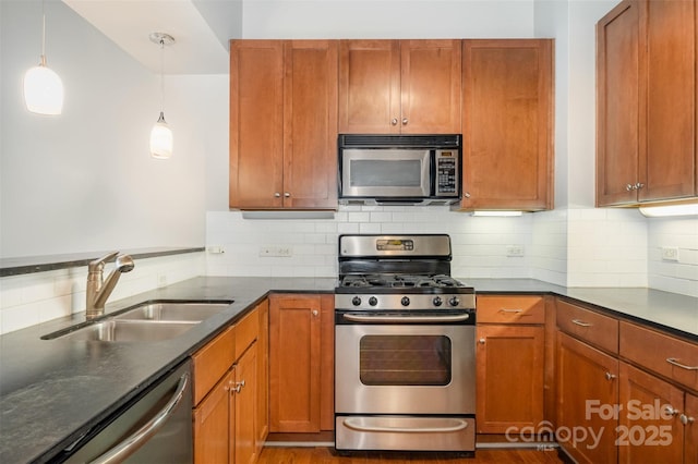 kitchen featuring appliances with stainless steel finishes, dark countertops, pendant lighting, and a sink