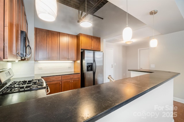 kitchen with hanging light fixtures, appliances with stainless steel finishes, brown cabinetry, and dark countertops