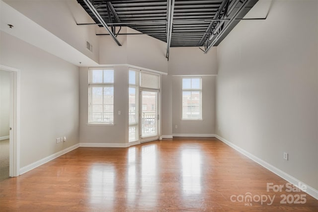 empty room featuring a towering ceiling, light wood-style flooring, visible vents, and baseboards