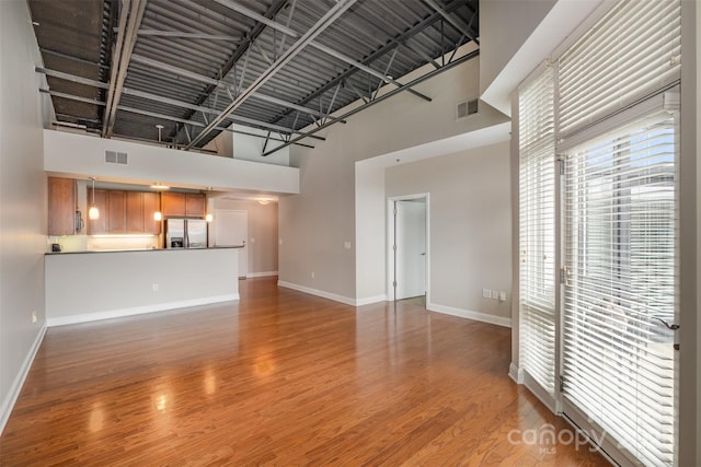 unfurnished living room with a high ceiling, light wood-type flooring, visible vents, and baseboards