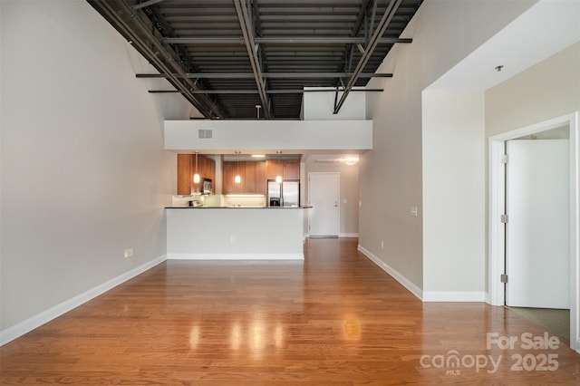 unfurnished living room with a towering ceiling, light wood finished floors, visible vents, and baseboards