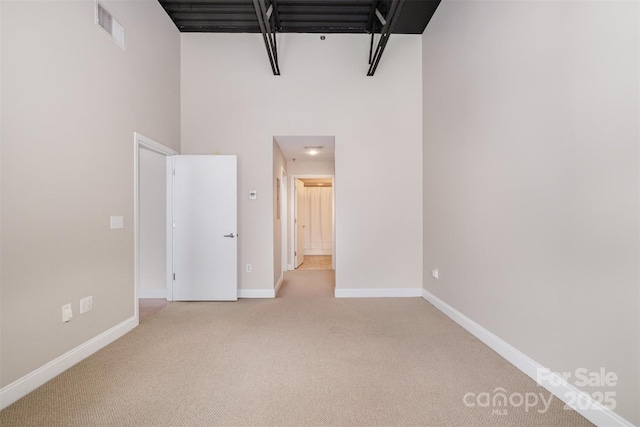 unfurnished bedroom featuring light colored carpet, visible vents, a towering ceiling, and baseboards