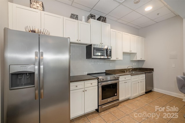 kitchen with light tile patterned floors, white cabinets, appliances with stainless steel finishes, a sink, and backsplash