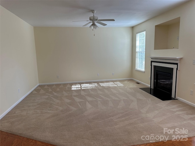 unfurnished living room featuring a fireplace with flush hearth, baseboards, ceiling fan, and light colored carpet