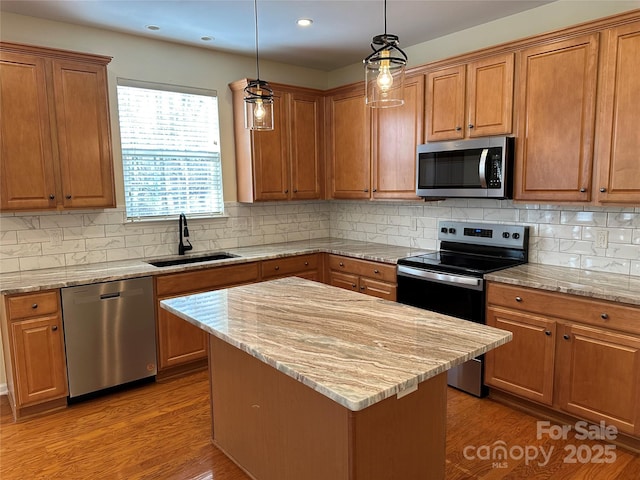 kitchen featuring decorative light fixtures, appliances with stainless steel finishes, a sink, a kitchen island, and light stone countertops