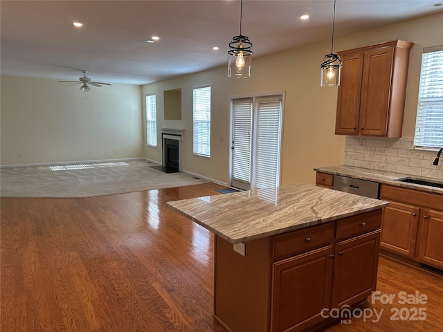 kitchen featuring light stone counters, a sink, a kitchen island, open floor plan, and brown cabinetry