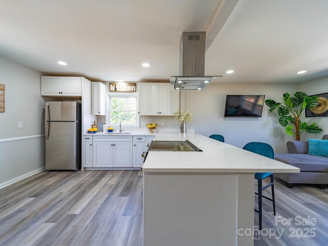 kitchen with island range hood, a peninsula, light countertops, freestanding refrigerator, and a kitchen bar