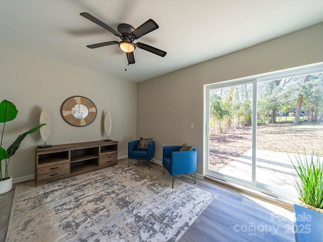 living area with a ceiling fan, baseboards, and wood finished floors