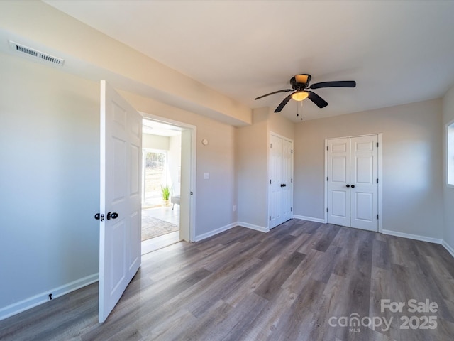 unfurnished bedroom featuring a ceiling fan, dark wood-style flooring, visible vents, and baseboards