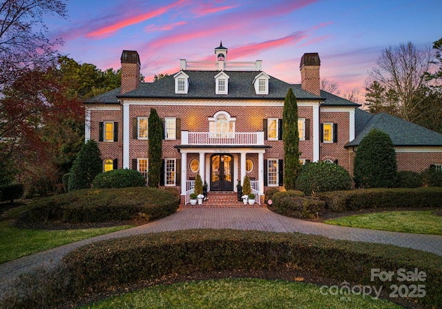 colonial-style house with decorative driveway, french doors, brick siding, a chimney, and a balcony