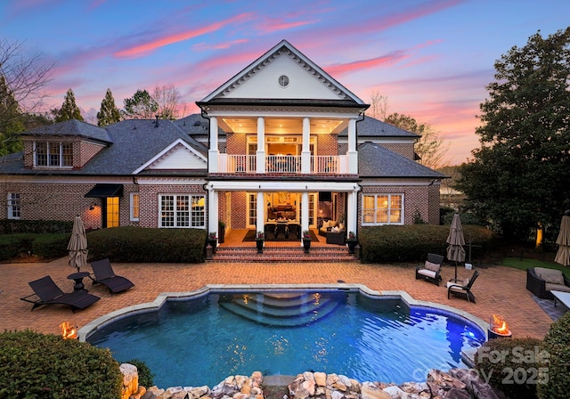 back of property featuring a balcony, a patio area, an outdoor pool, and brick siding