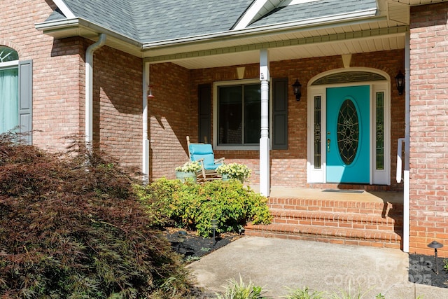 property entrance featuring covered porch, roof with shingles, and brick siding