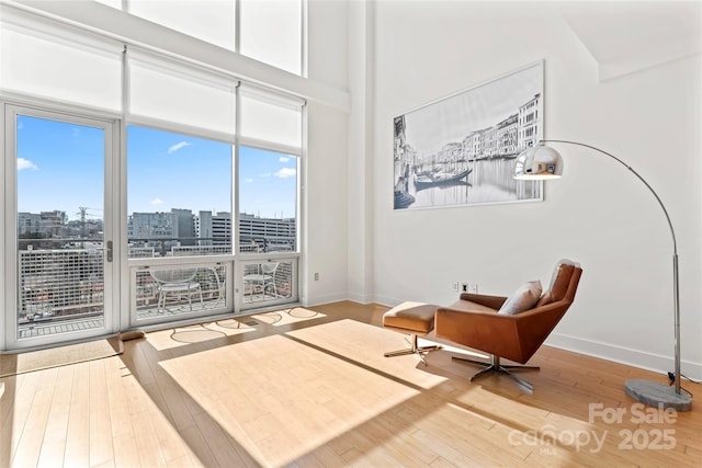 sitting room featuring a view of city, a high ceiling, hardwood / wood-style flooring, and baseboards