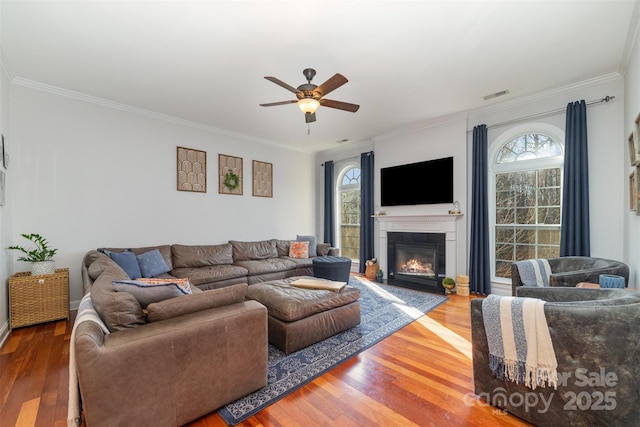 living room with crown molding, visible vents, wood finished floors, and a glass covered fireplace