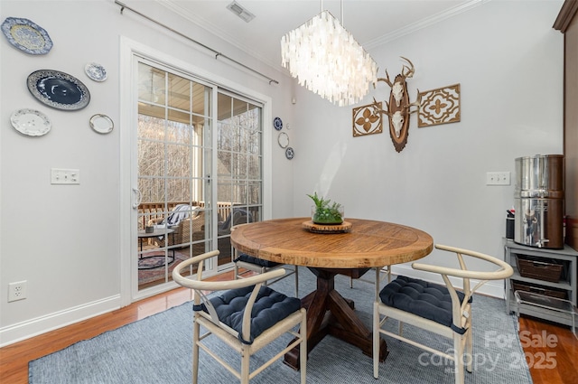 dining space featuring dark wood-style flooring, visible vents, an inviting chandelier, ornamental molding, and baseboards