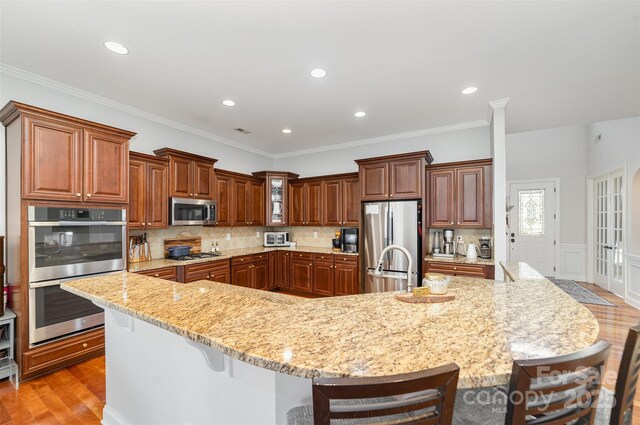 kitchen featuring stainless steel appliances, a breakfast bar, a spacious island, wood finished floors, and light stone countertops