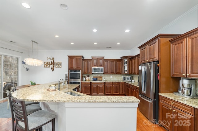 kitchen featuring pendant lighting, brown cabinets, appliances with stainless steel finishes, a sink, and an island with sink