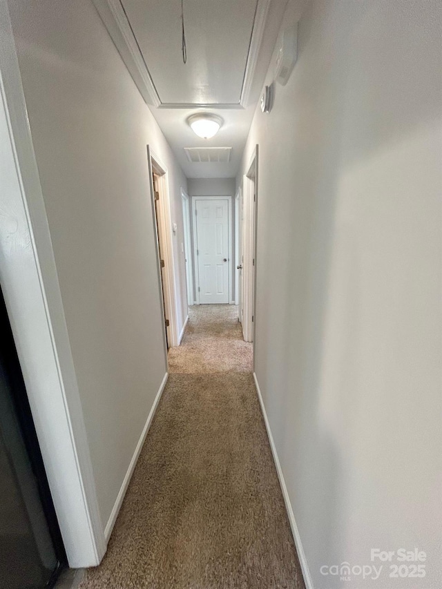 corridor with attic access, light colored carpet, and baseboards