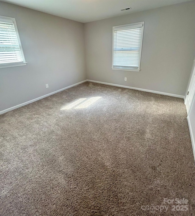 unfurnished room featuring carpet floors, visible vents, and baseboards