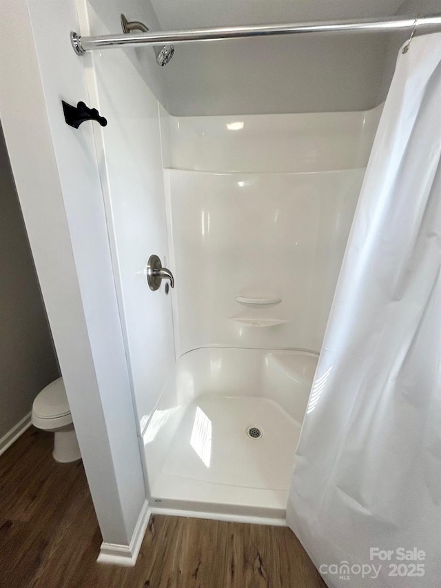 full bathroom featuring toilet, a stall shower, and wood finished floors