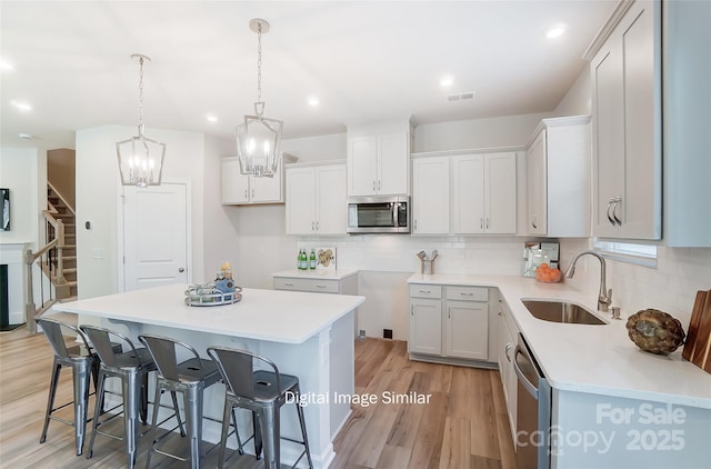 kitchen with light countertops, appliances with stainless steel finishes, white cabinetry, a kitchen island, and a sink